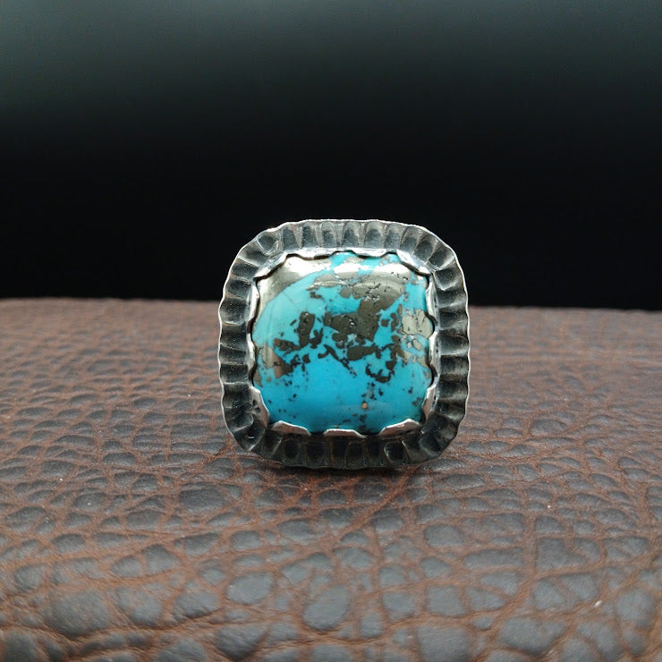 Stamped sterling silver ring band on ring mandrel showing thunderbird and geometric motifs, oxidized finish detail