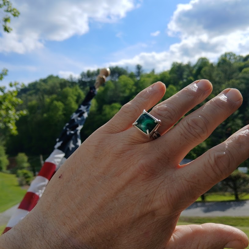 Green stone ring on hand with American flag and trees in background