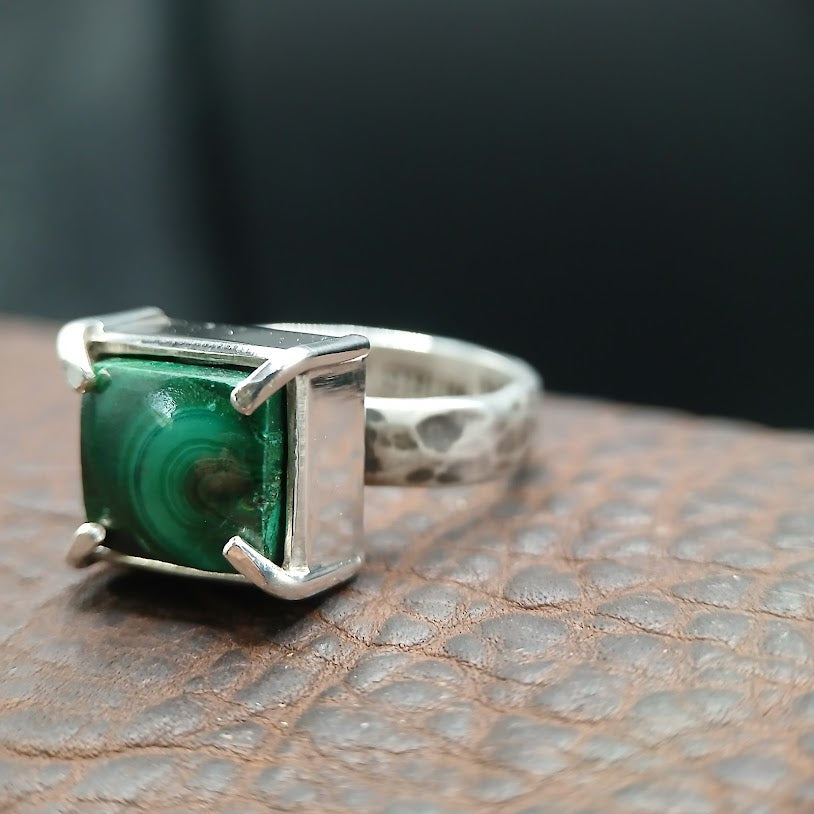 Silver ring with a green stone on a textured surface