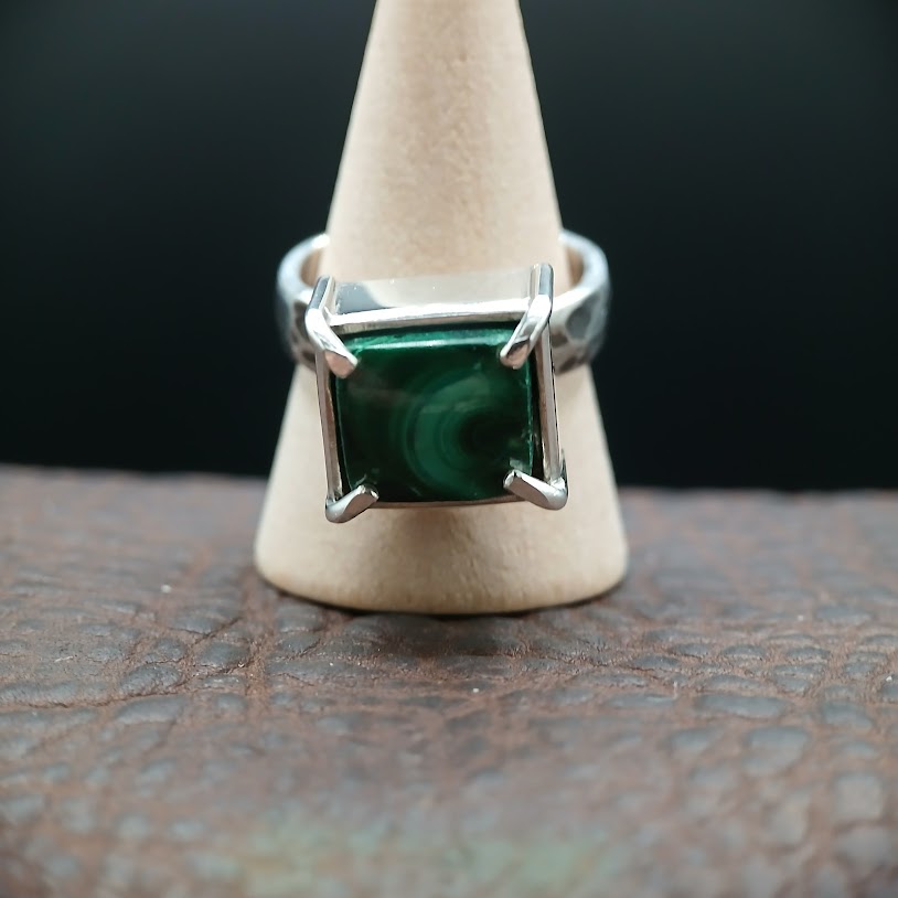 Ring with a green gemstone on a wooden stand against a dark background