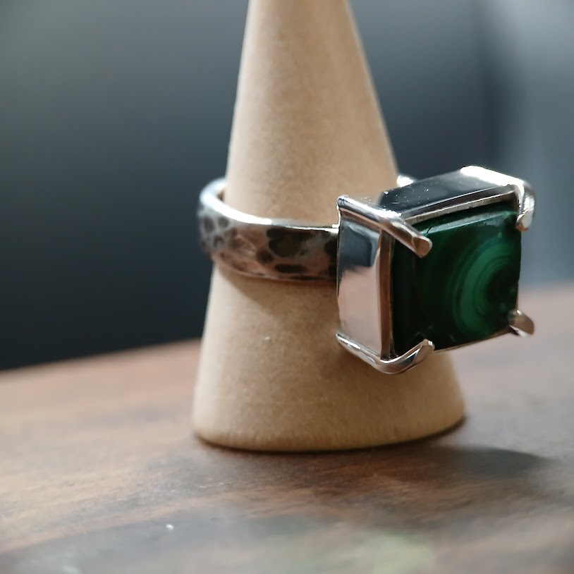Silver ring with a green gemstone on a wooden stand against a dark background