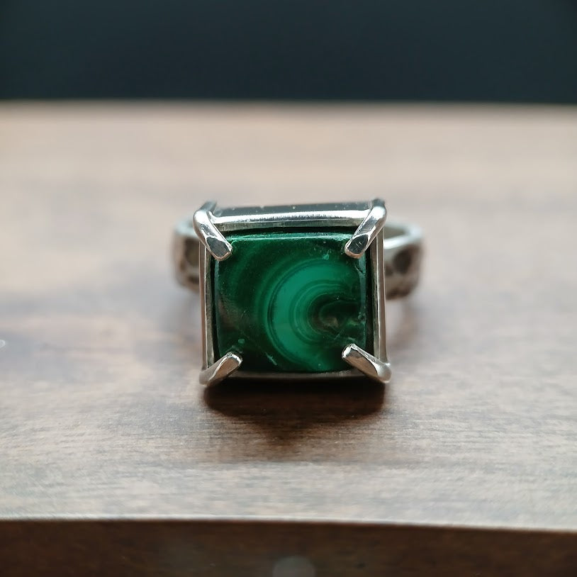 Ring with a green gemstone and silver setting on a wooden surface