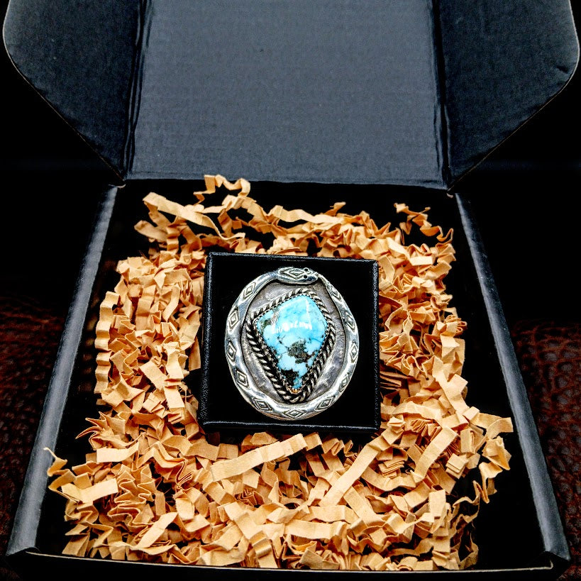 Silver ring with turquoise stone in a black box with shredded brown paper