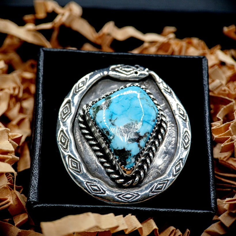 Silver ring with a blue stone on a black box against a brown textured background