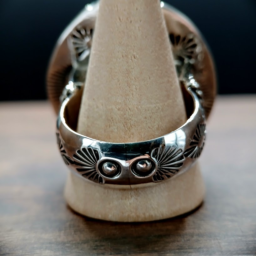 Silver ring with intricate designs on a wooden stand against a dark background