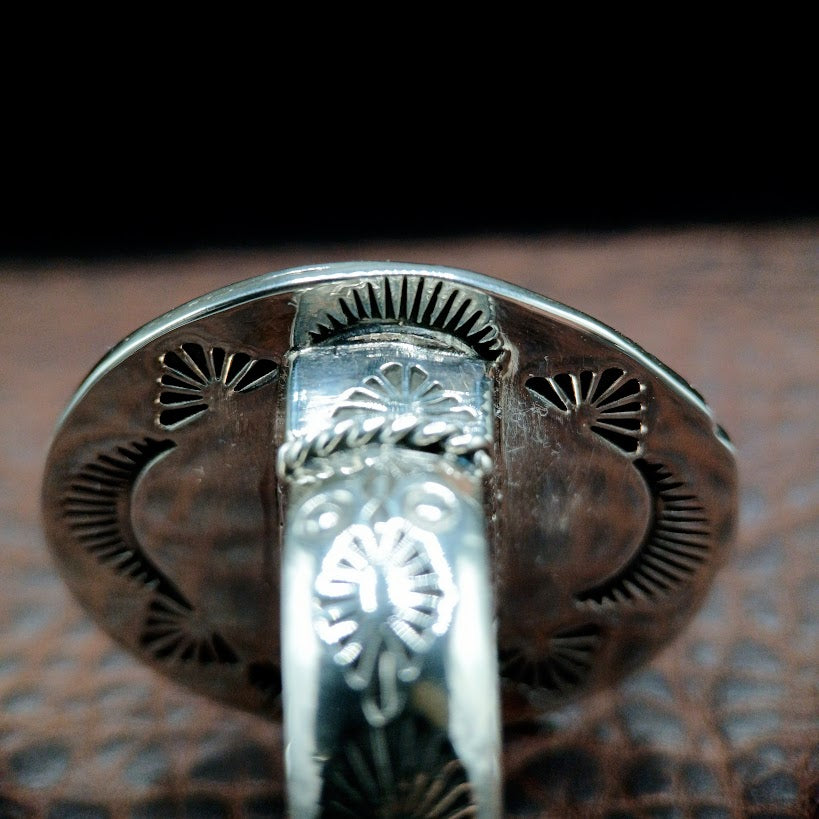 Close-up of a silver ring with intricate designs on a textured surface