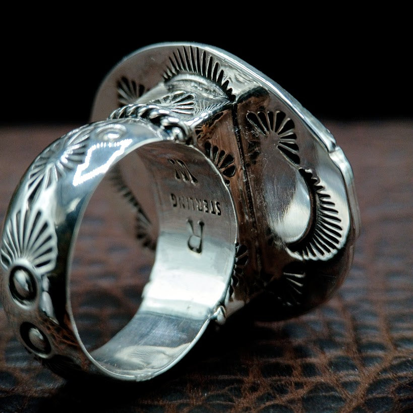 Silver ring with intricate designs on a dark textured surface