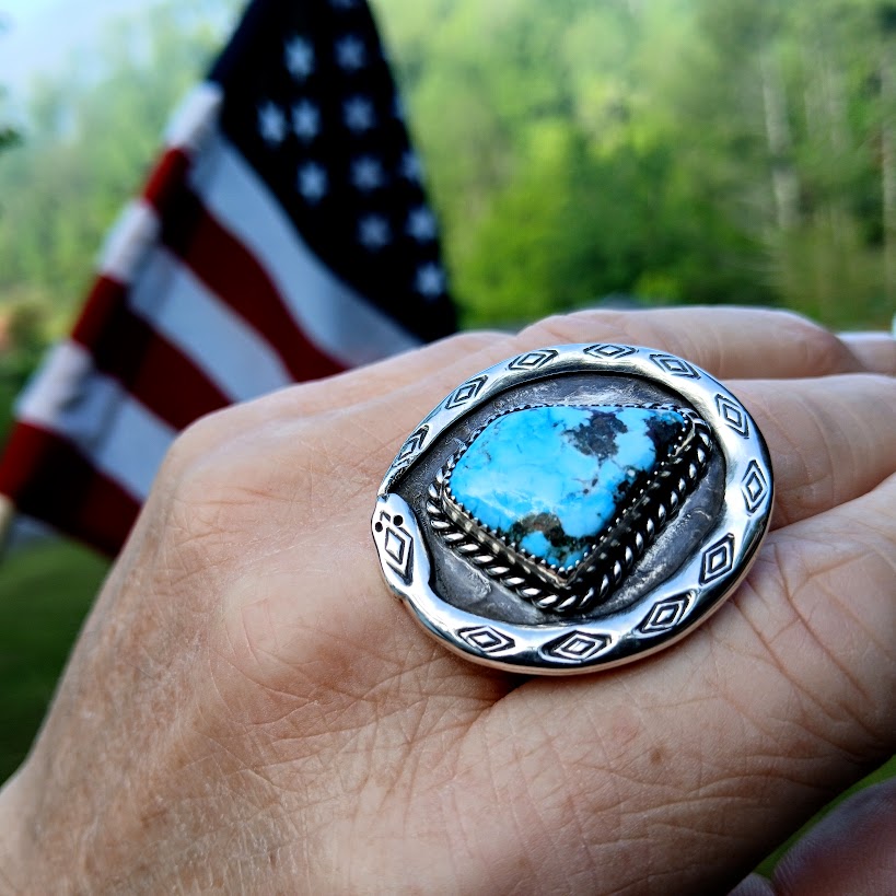 Silver ring with a blue stone on a hand, American flag in the background