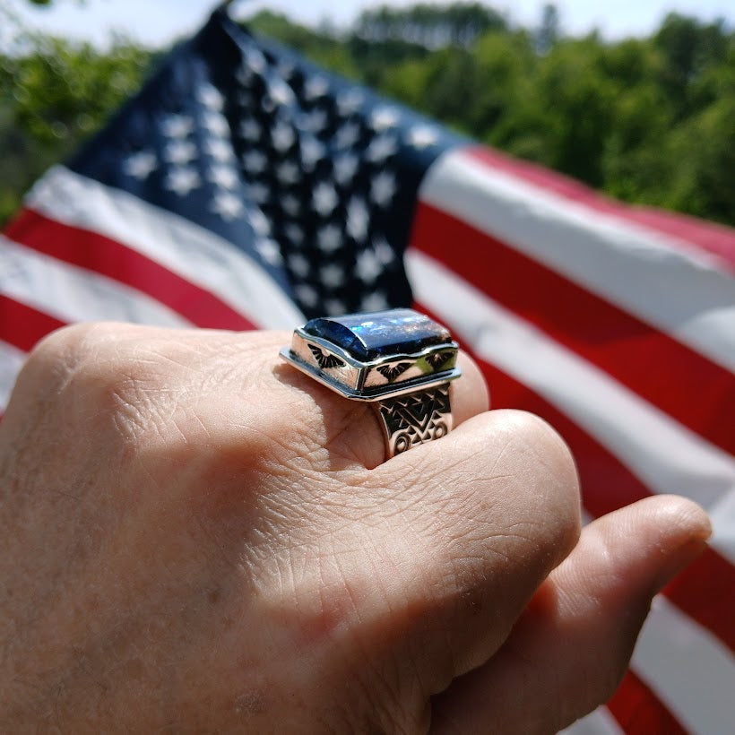 Hand wearing a ring with an American flag in the background