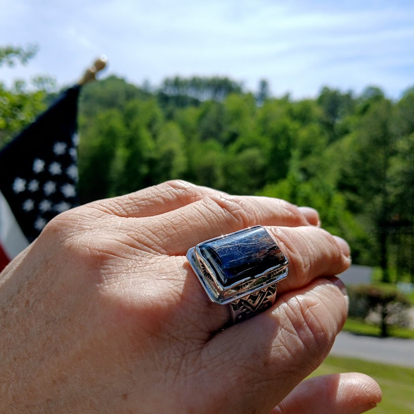 Hand wearing a ring with a blue stone against a blurred outdoor background