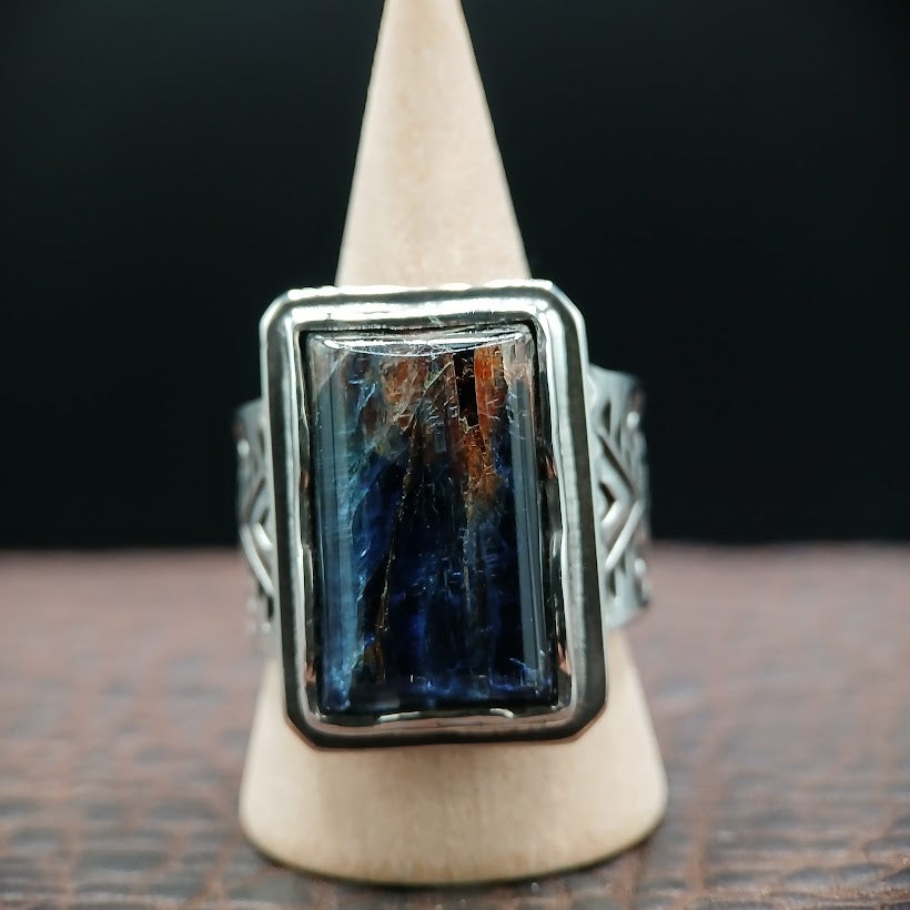 Silver ring with a rectangular blue stone on a wooden stand against a dark background