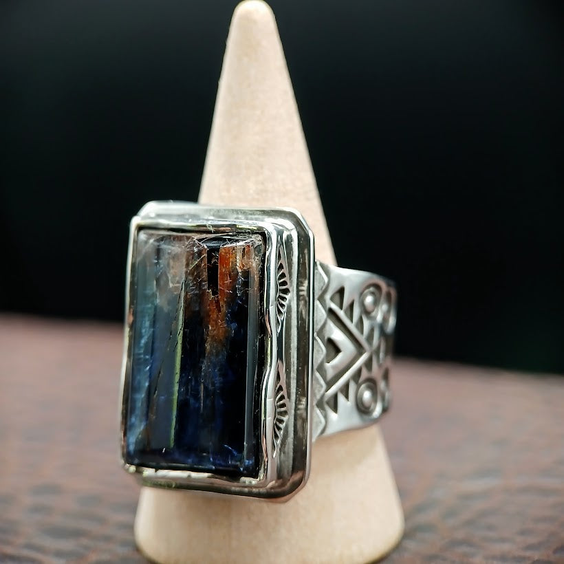 Silver ring with a rectangular stone on a wooden stand against a dark background
