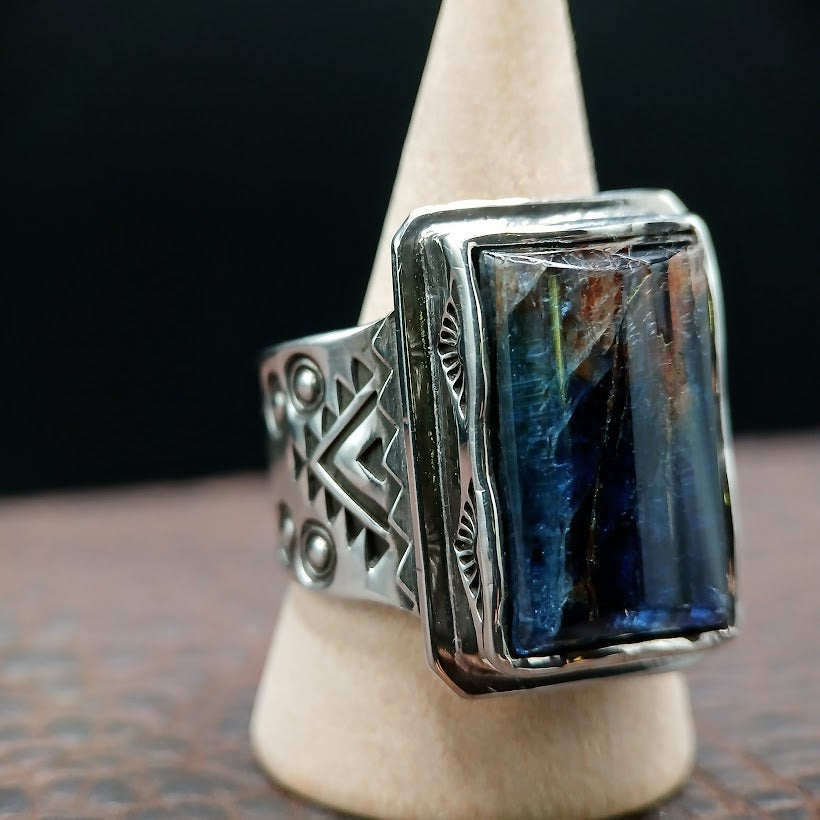 Silver ring with blue stone on a wooden stand against a dark background