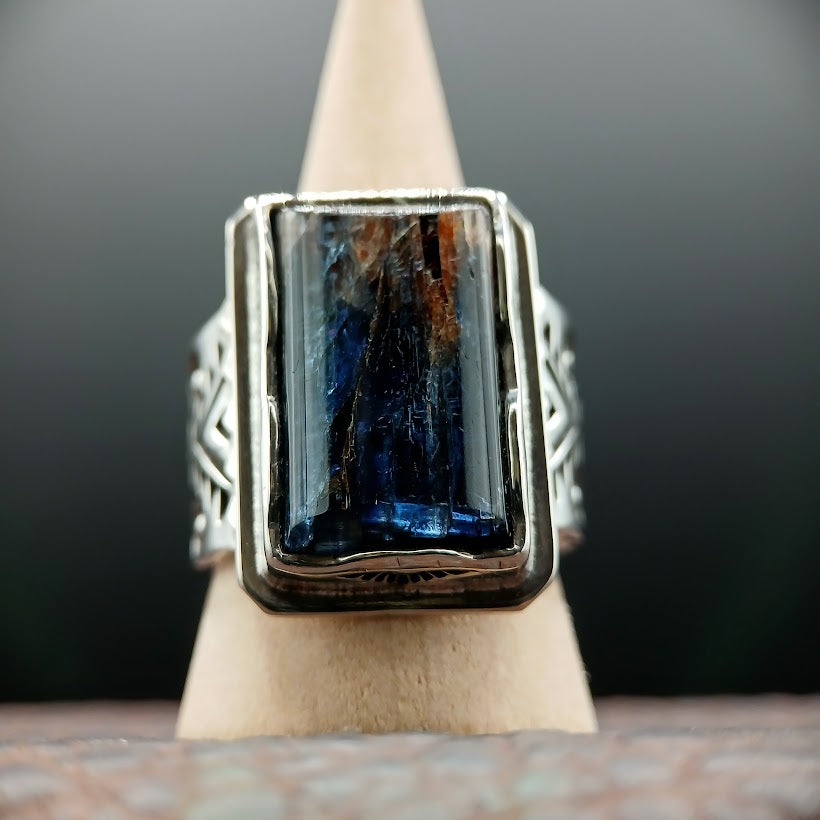 Silver ring with a blue gemstone on a wooden stand against a dark background