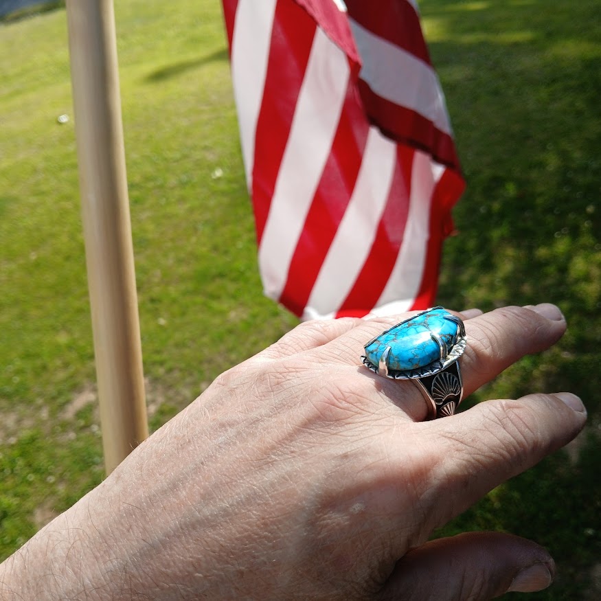 Hand wearing a turquoise ring with an American flag in the background