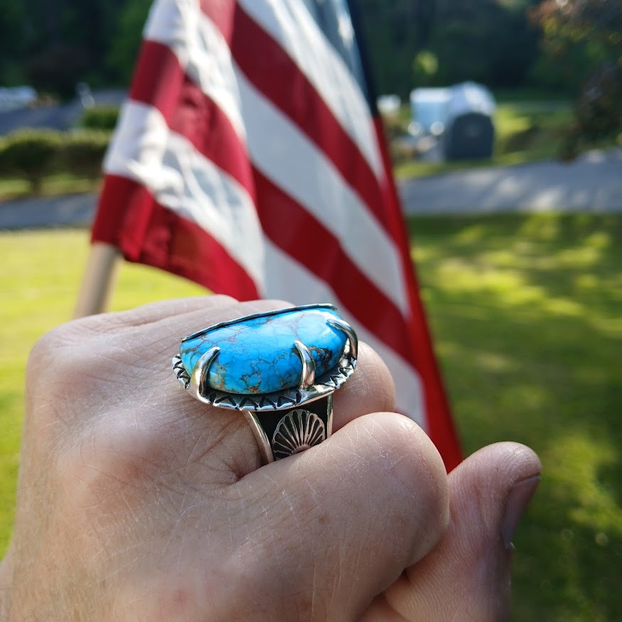Hand wearing a turquoise ring with an American flag in the background