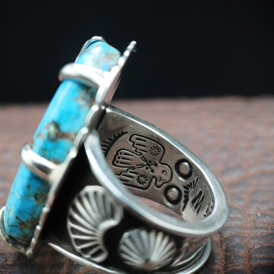 Silver ring with turquoise stone on a dark background with thunderbird stamping inside of the band