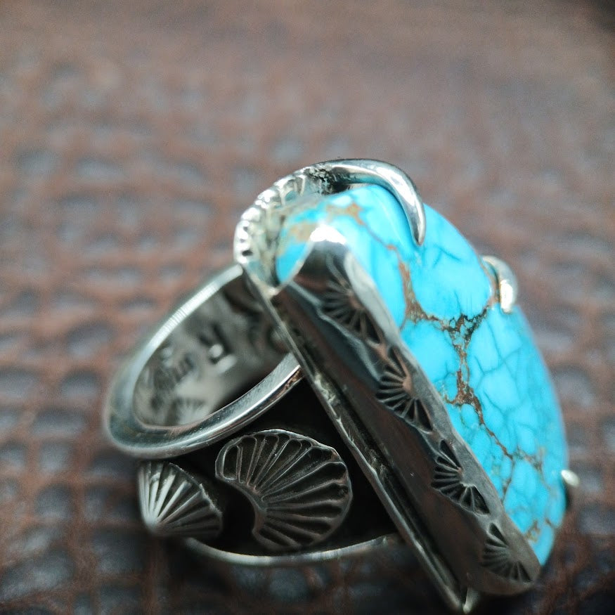 Turquoise ring with silver band on a textured brown background