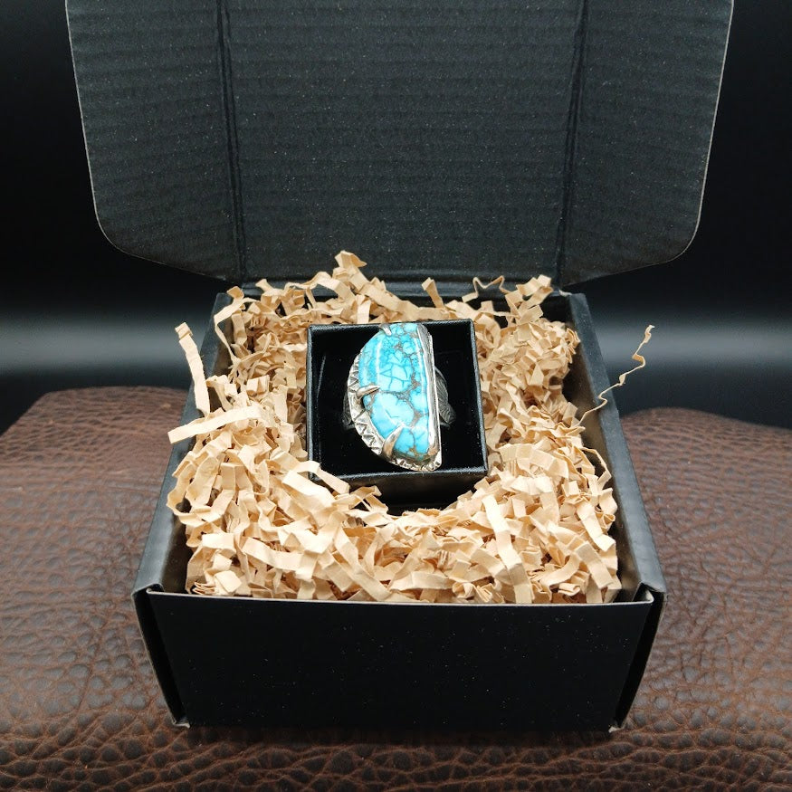 Turquoise ring in a black box with gold interior on a brown leather surface