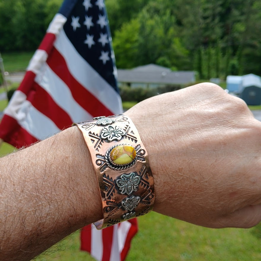Copper bracelet with a yellow stone on a wrist in front of an American flag.