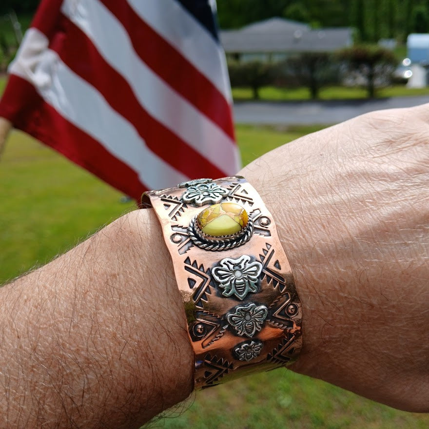 Copper bracelet with intricate designs on a wrist, American flag in the background