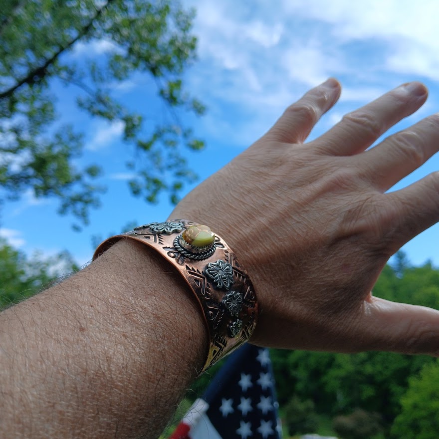 Hand wearing a decorative copper bracelet with a blurred natural background