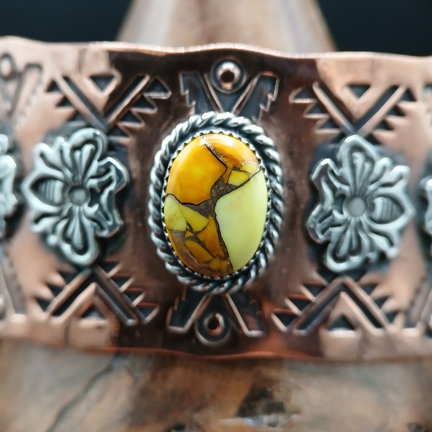 Decorative cuff bracelet with a yellow gemstone and bee patterns on a dark background