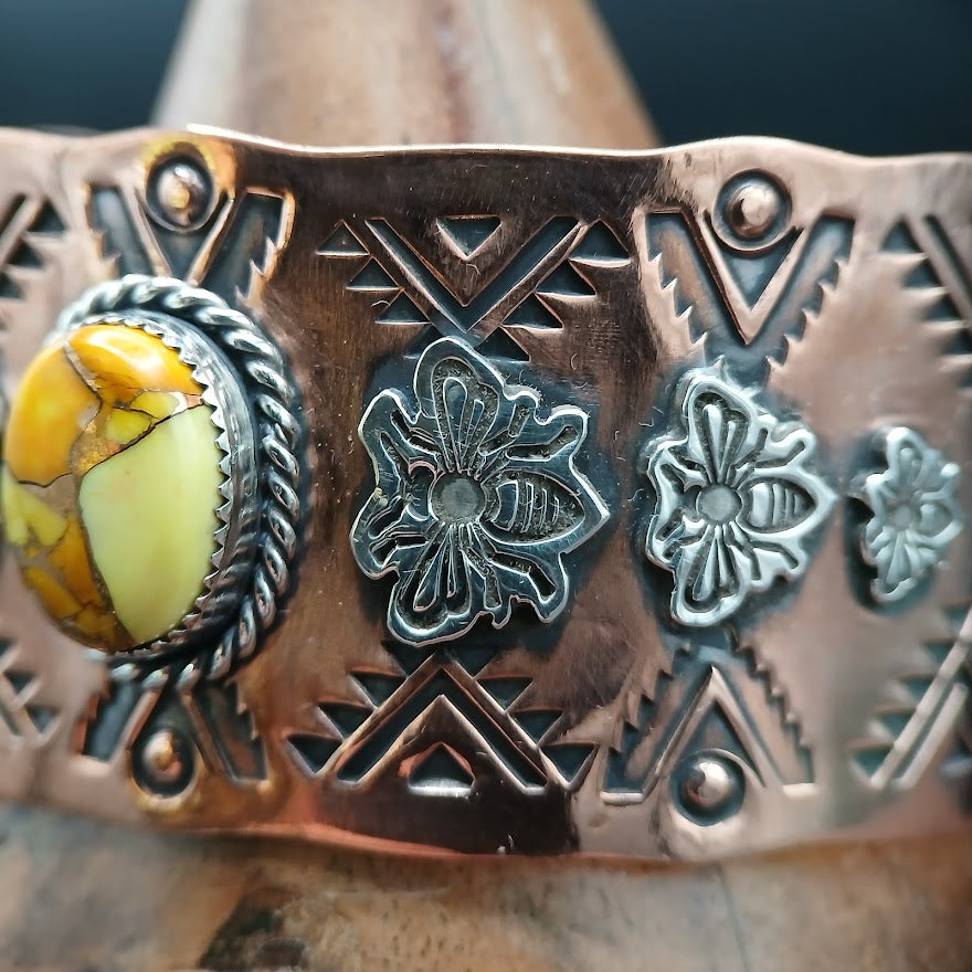 Close-up of a copper bracelet with intricate designs and a central stone.