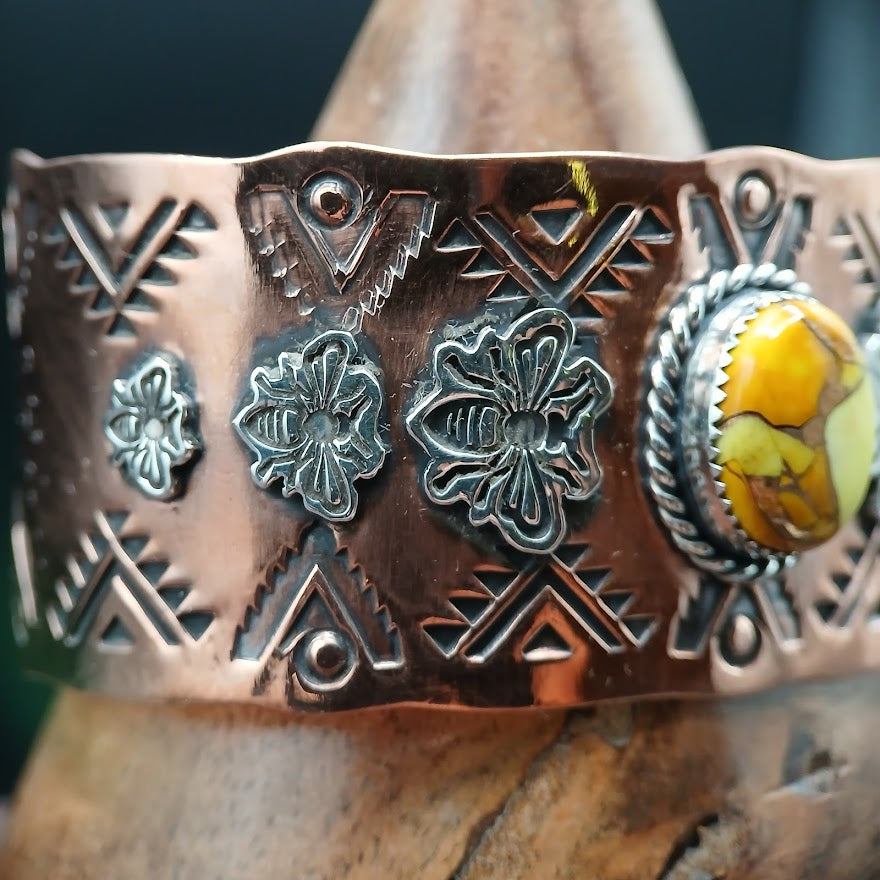 Copper bracelet with honey bee designs and a yellow stone on a wooden surface.