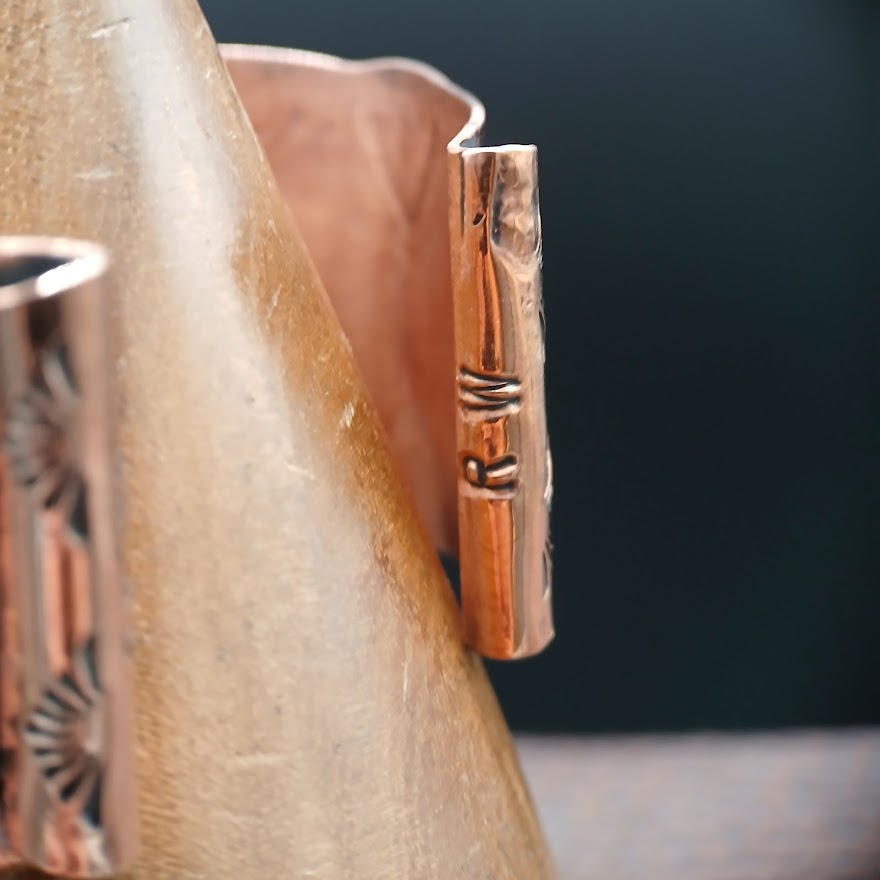 Close-up of a metallic object with intricate design on a dark background, hallmarked with RW