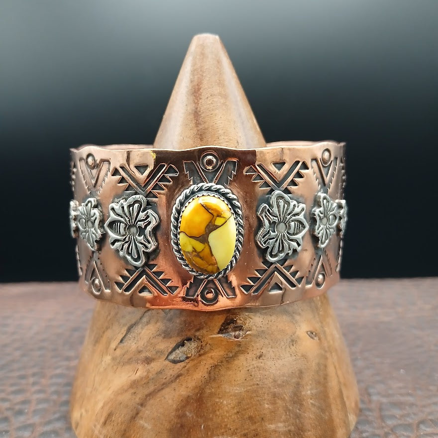 Copper bracelet with decorative elements and a yellow stone on a wooden stand against a dark background