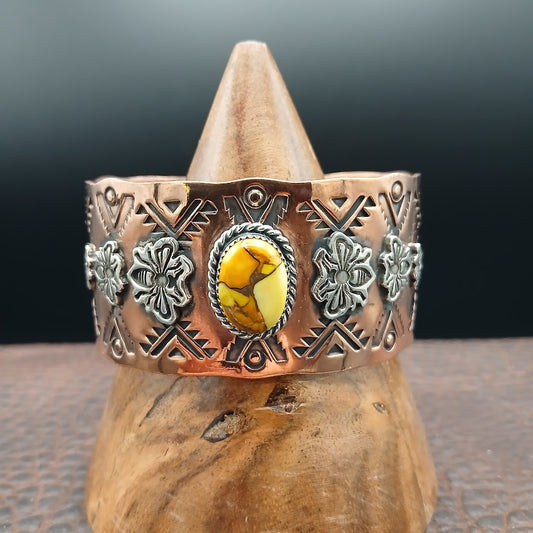 Copper bracelet with decorative elements and a yellow stone on a wooden stand against a dark background