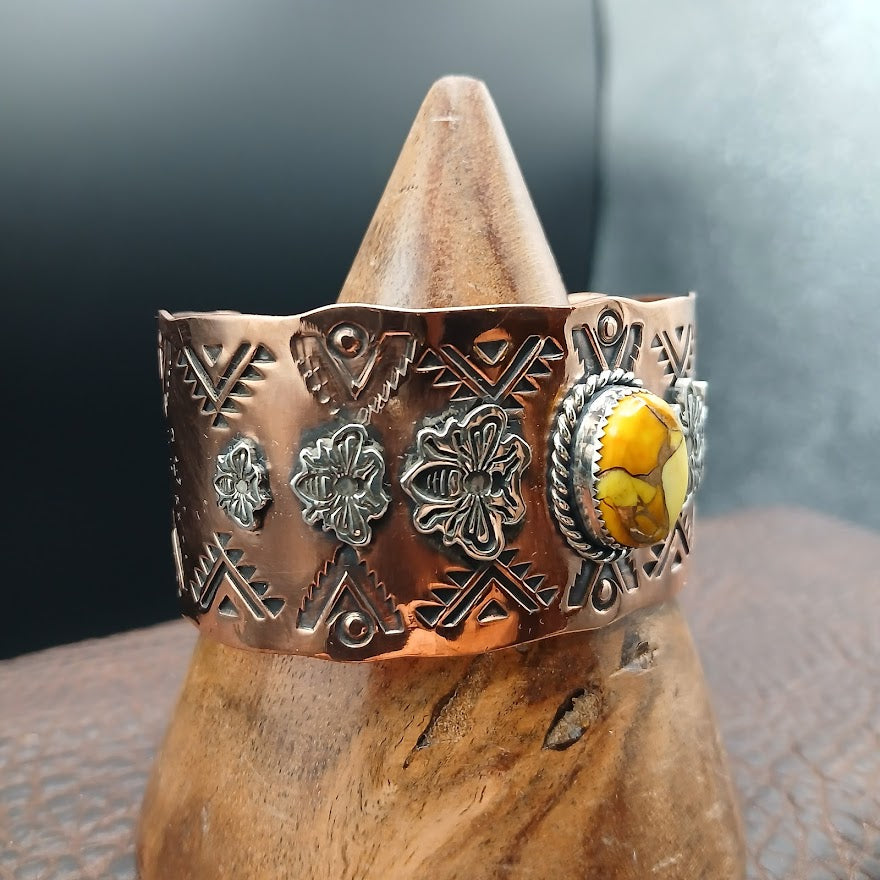 Decorative copper bracelet with a yellow stone on a wooden stand against a dark background