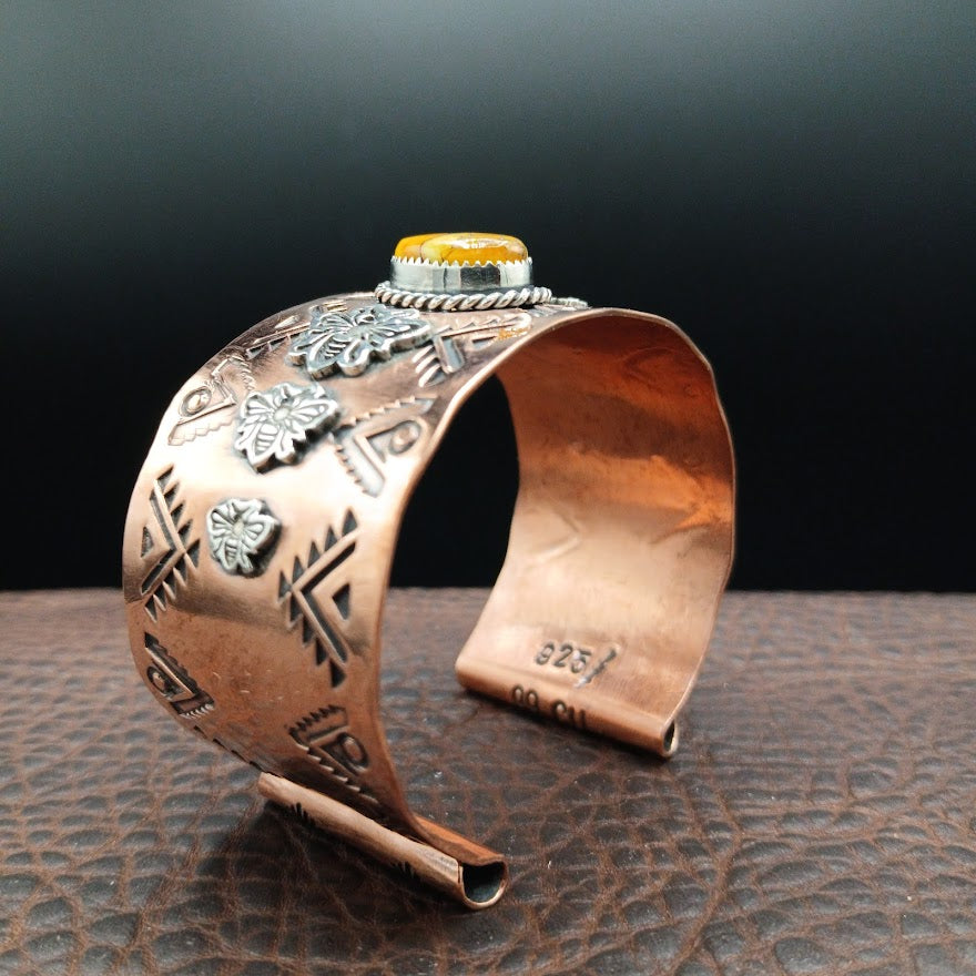 Copper cuff bracelet with intricate designs on a dark background