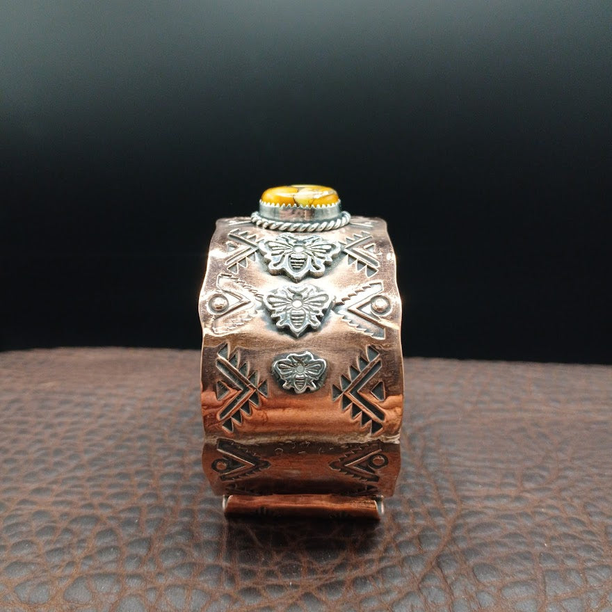 Decorative copper cuff bracelet with intricate designs on a textured surface