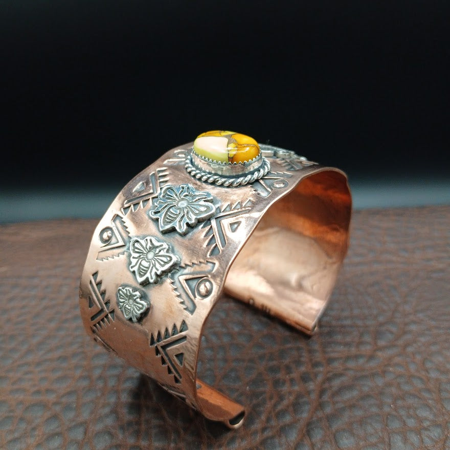 Copper bracelet with intricate designs and a yellow stone on a textured leather surface.