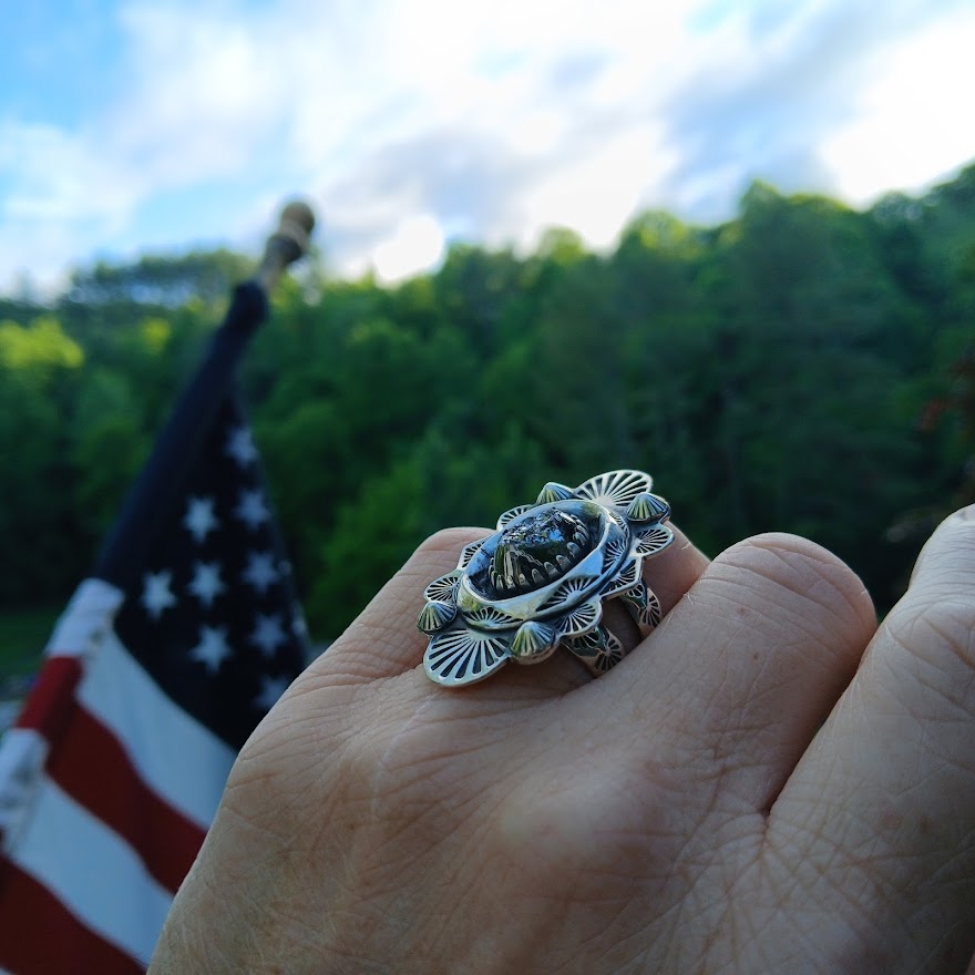 Hand wearing a decorative ring with an American flag in the background