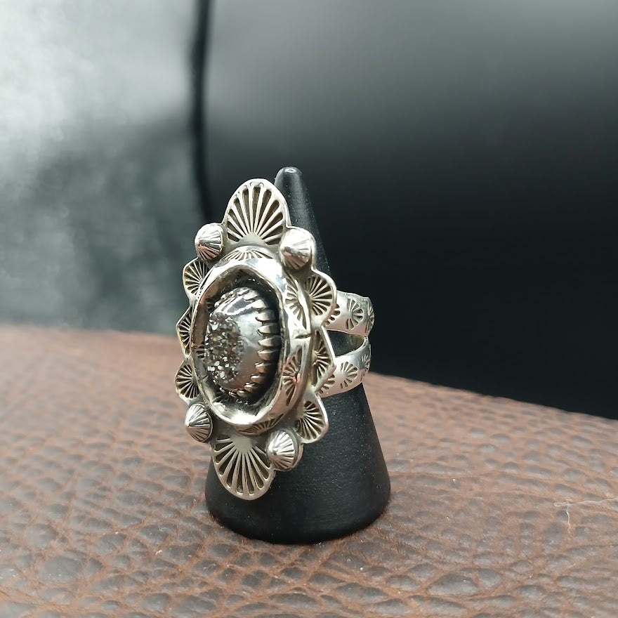Silver ring with intricate design on a black stand against a dark background