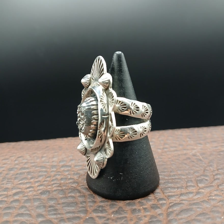 Silver ring with intricate design on a black stand against a dark background