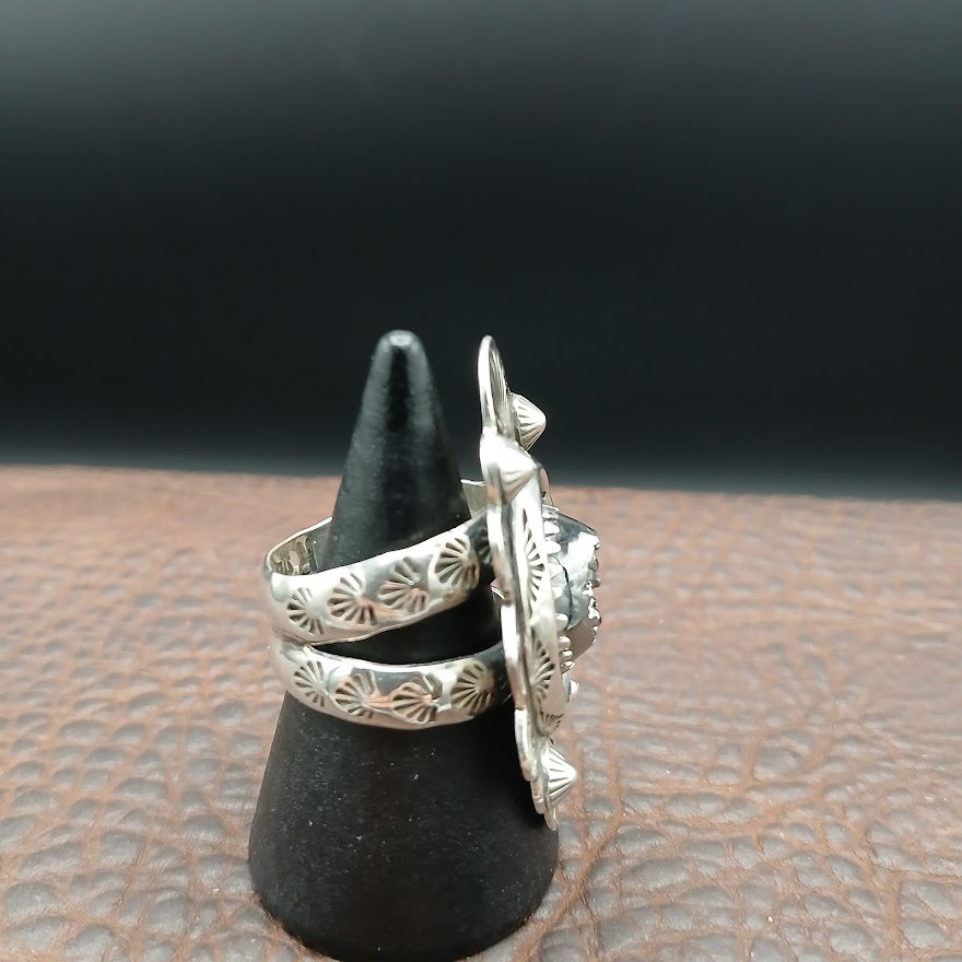 Silver ring with intricate design on a black cone-shaped stand against a dark background