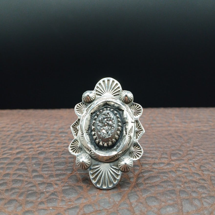 Silver ring with intricate design on a textured surface