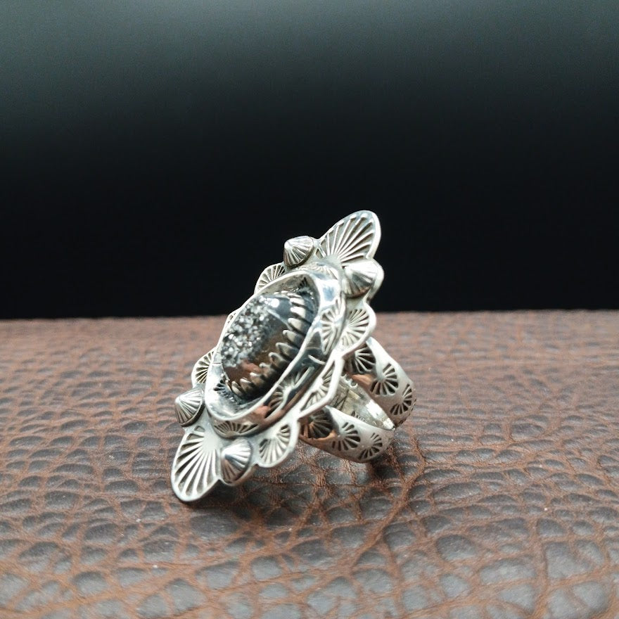 Silver ring with intricate design on a textured surface