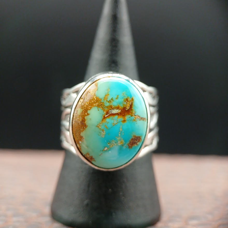 Turquoise ring with silver band on a black stand against a dark background