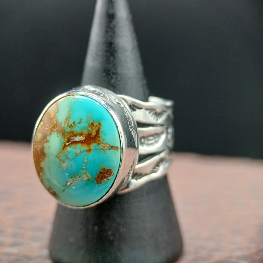 Turquoise ring with silver band on a black stand against a dark background