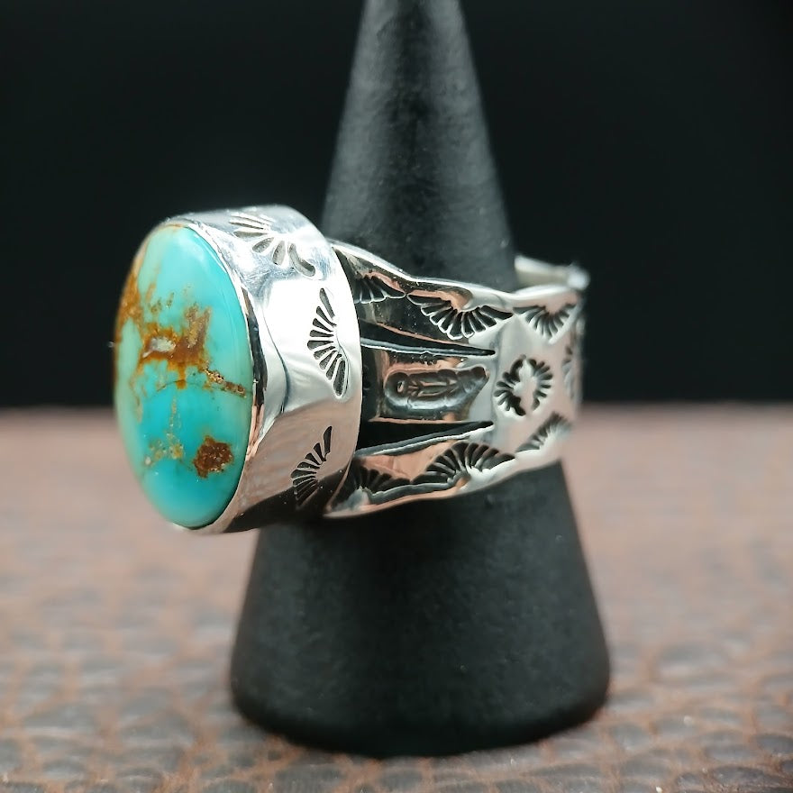 Silver ring with turquoise stone on a black stand against a dark background