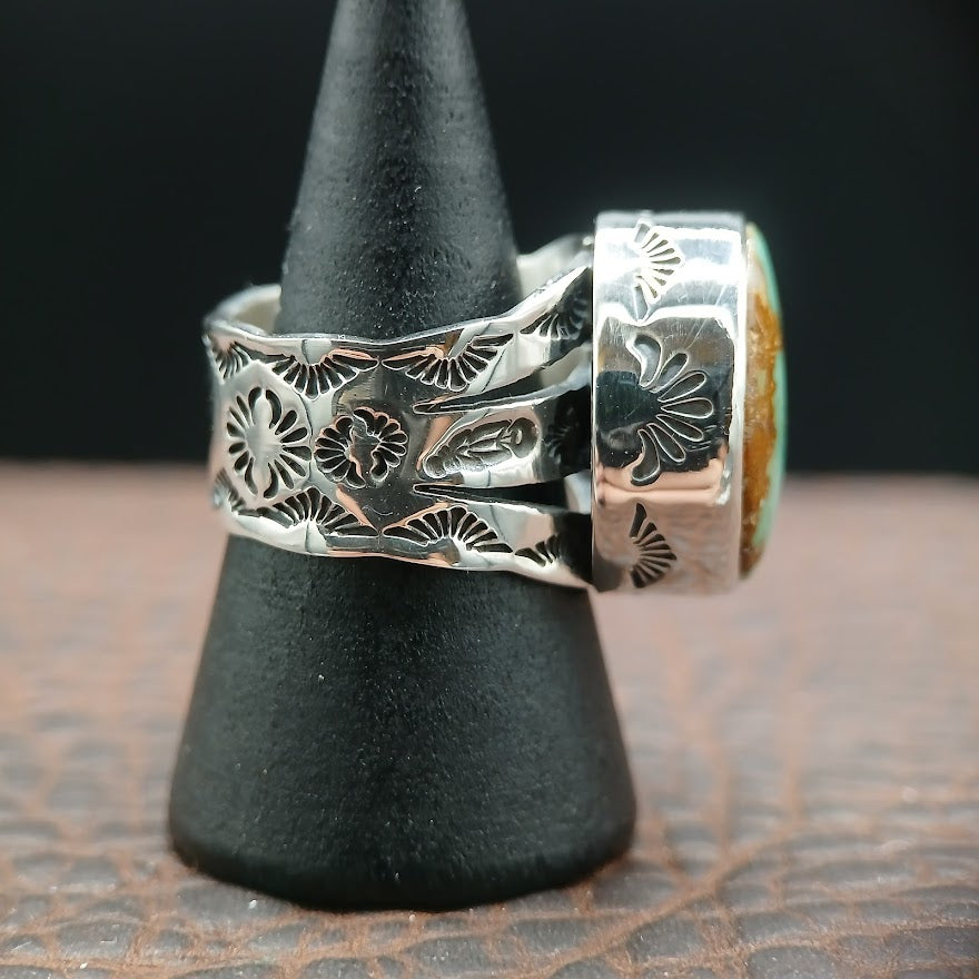 Silver ring with intricate designs on a black stand against a dark background