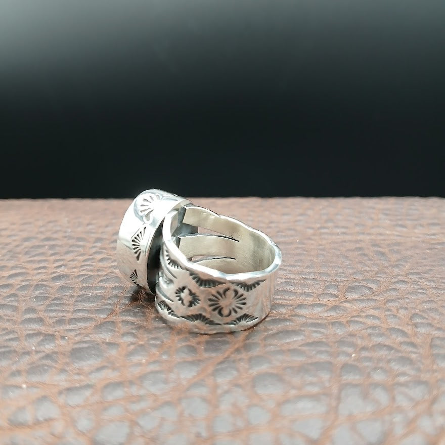 Silver ring with intricate designs on a textured surface
