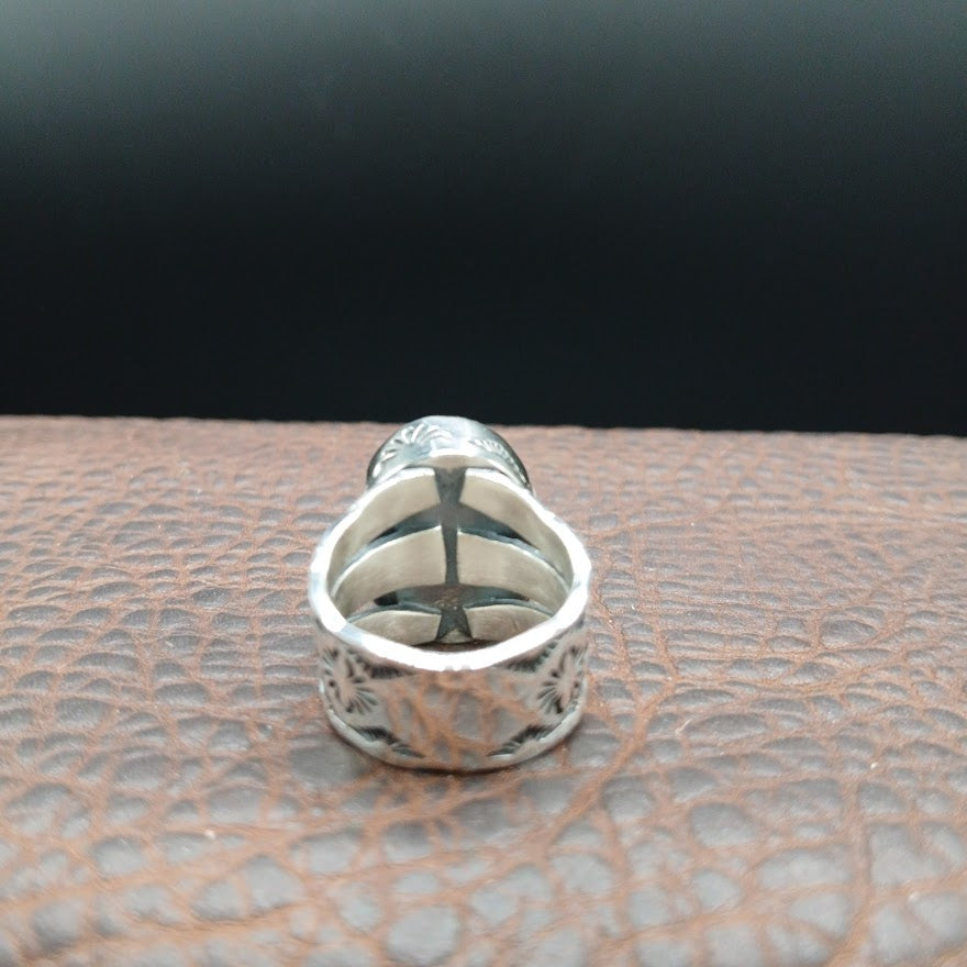 Silver ring with intricate design on a textured surface
