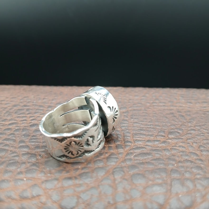 Silver ring with intricate designs on a textured surface