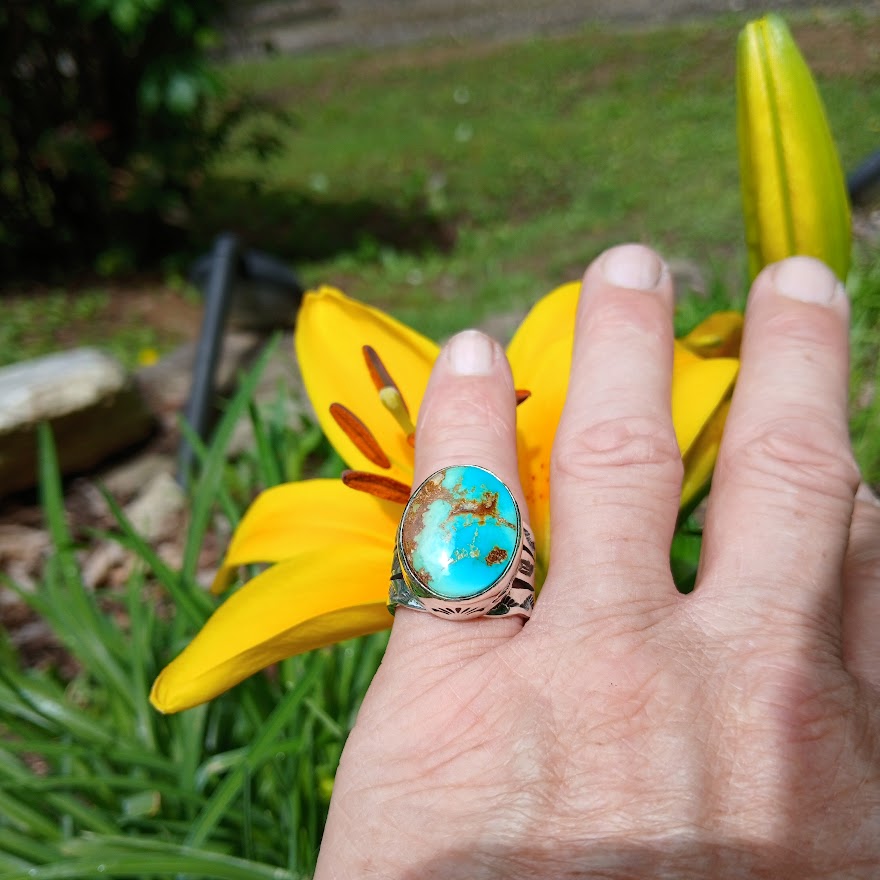Hand wearing a turquoise ring with a yellow flower in the background